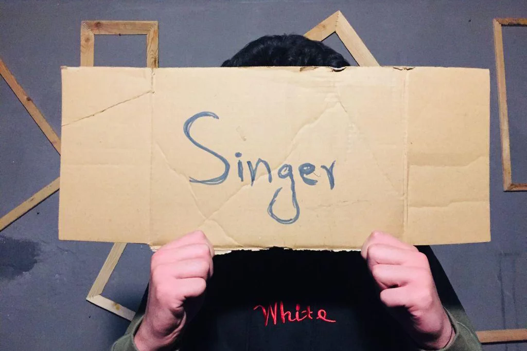 A person holding a sign in their hands that says "Singer"